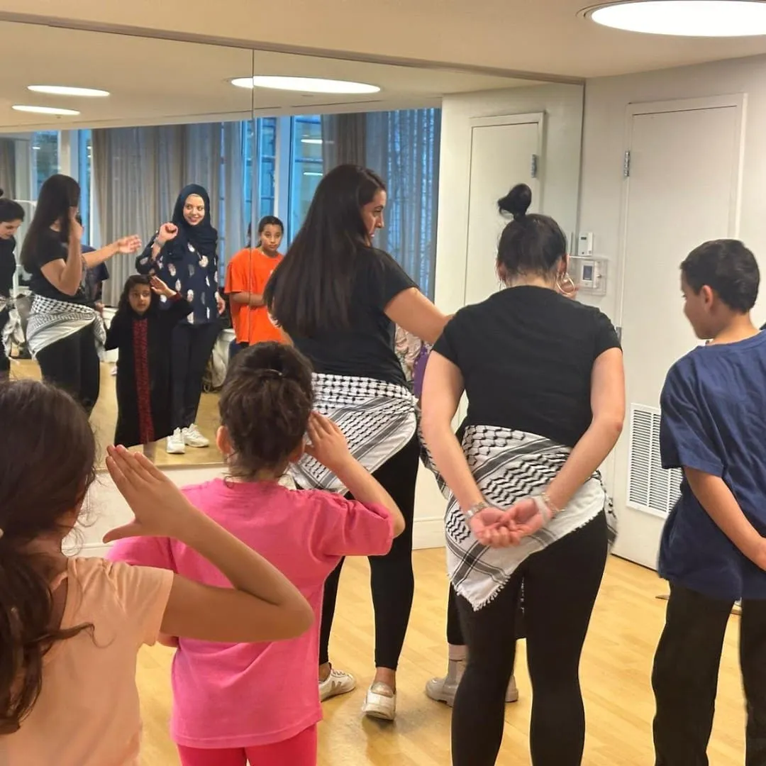 “A group of children and instructors participating in a dance or movement class in a mirrored studio, following steps together.”